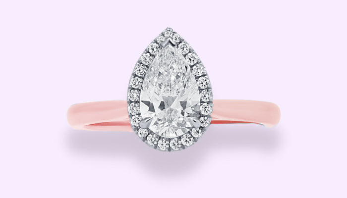 A pear shaped halo style diamond engagement ring with a rose gold band