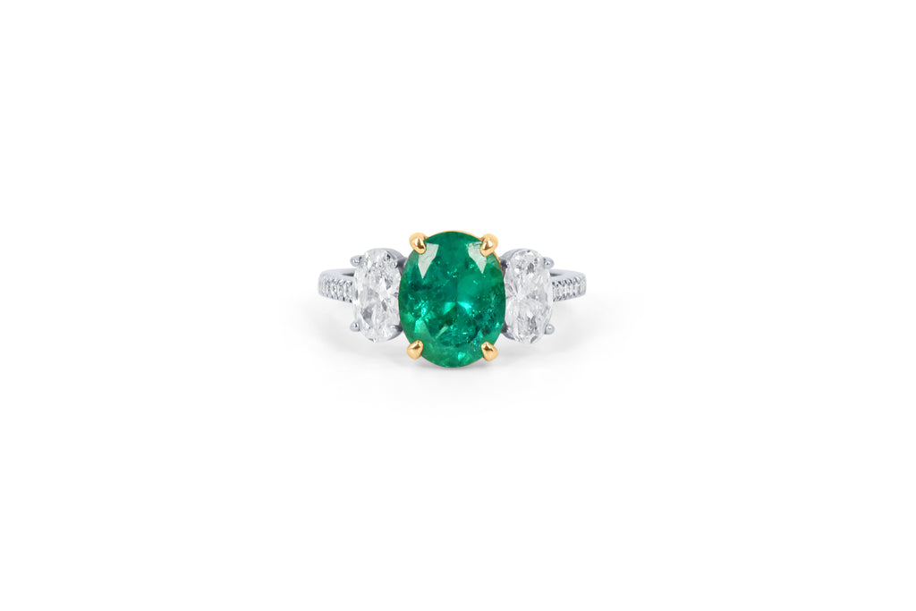 Diamond and emerald trilogy engagement ring with an oval emerald at the centre and two oval diamonds on each side, also with a diamond band