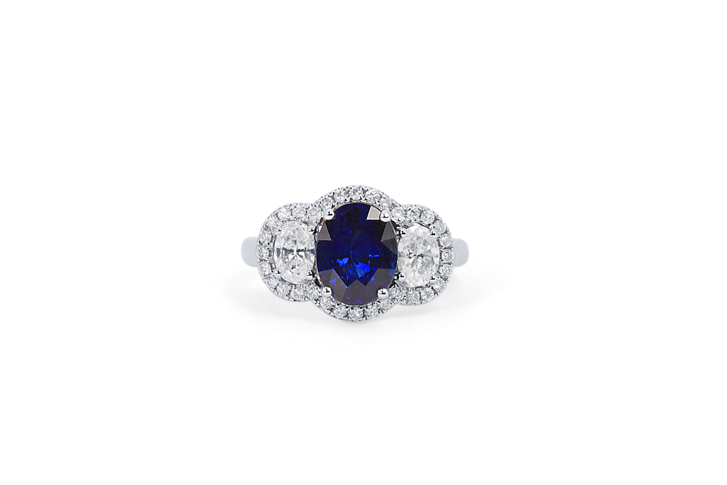 A custom bespoke diamond and sapphire halo engagement ring with an oval sapphire at the centre and two oval diamonds on the sides 