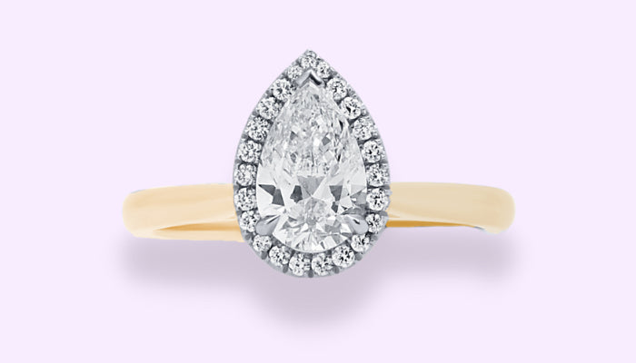 A pear shaped halo style diamond engagement ring with a yellow gold band